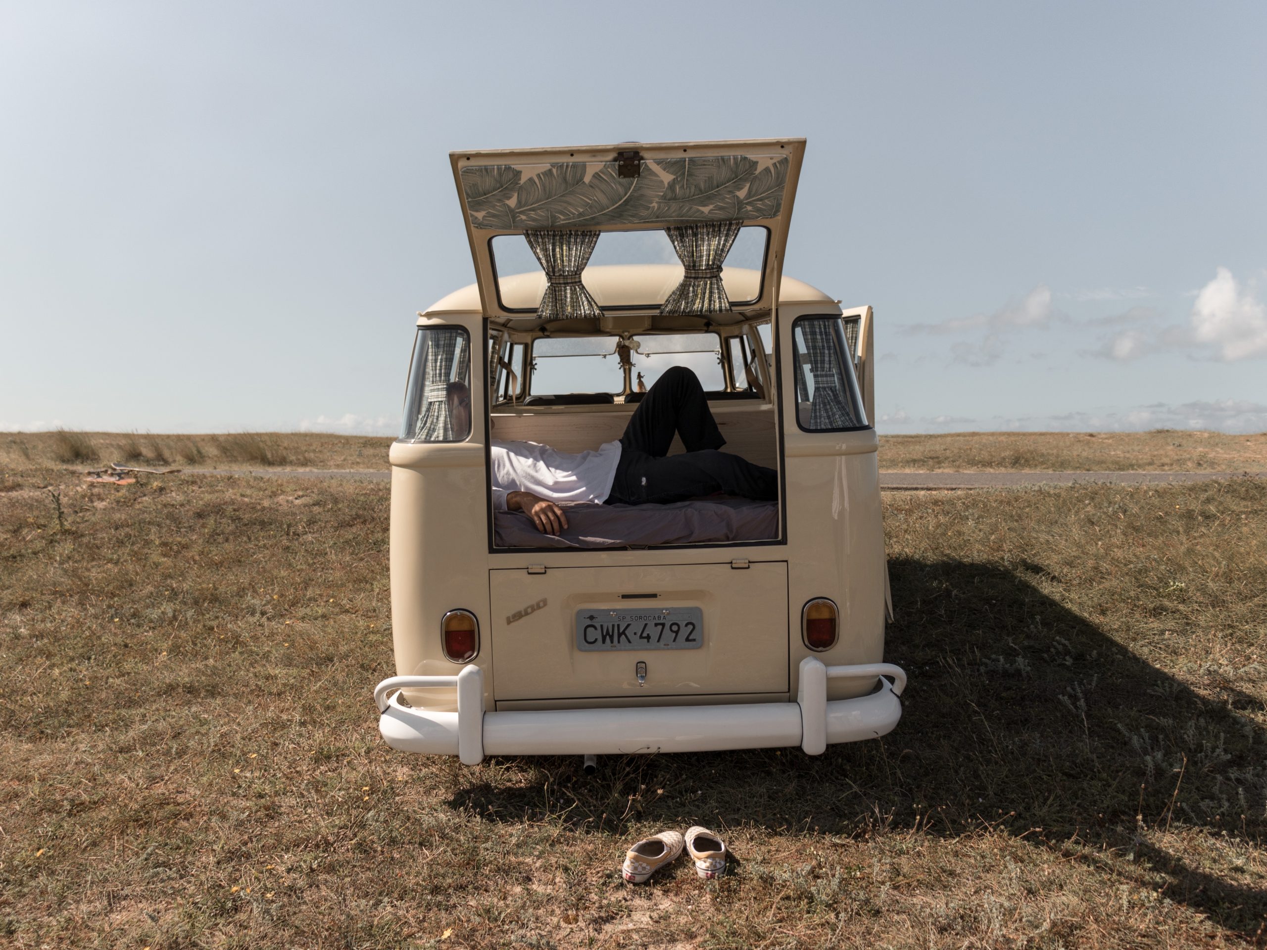 back of campervan with back door open showing double bed at back with man relaxing on the bed