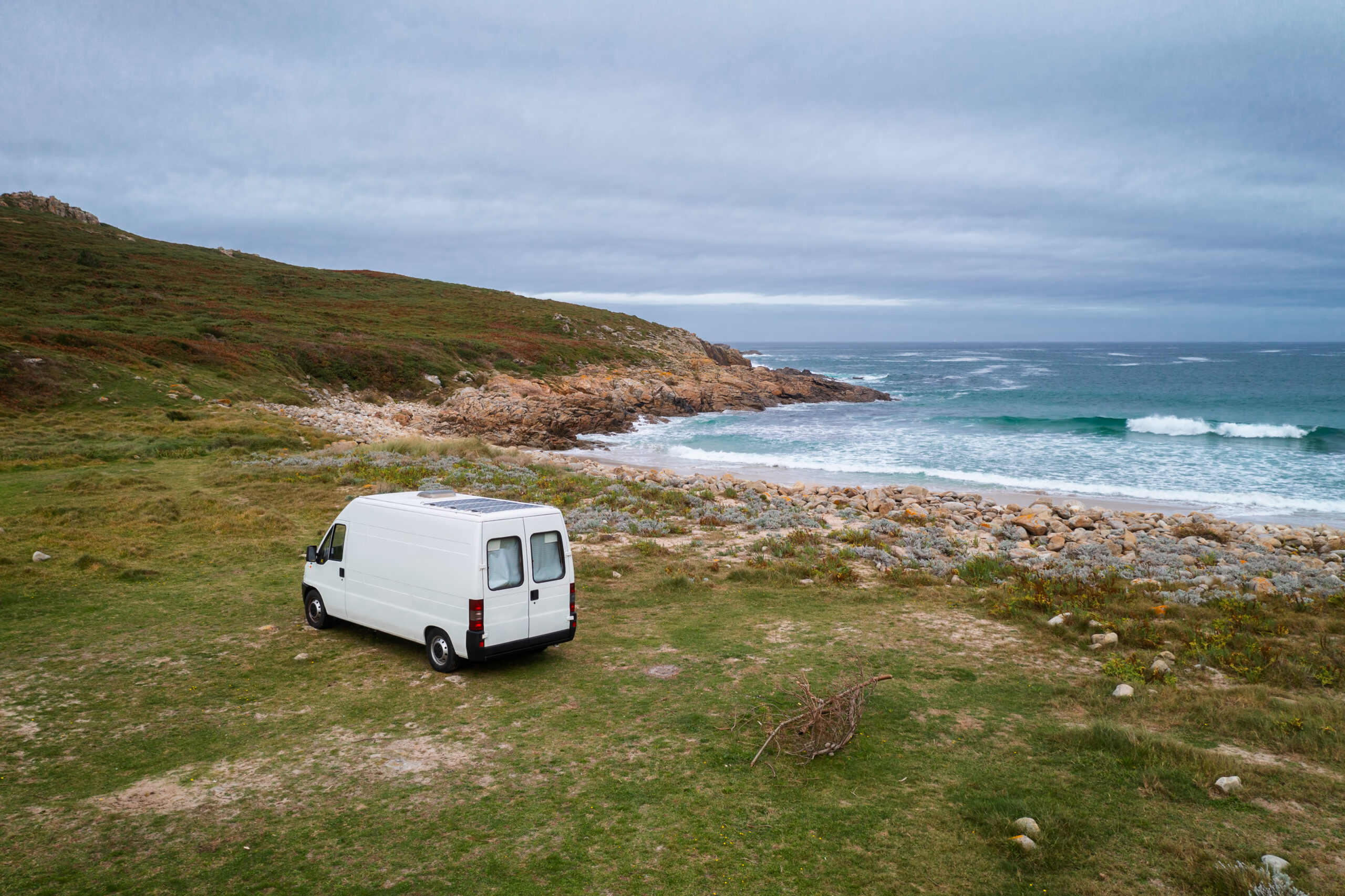 White camper van on a wild beach, parked up on the grass