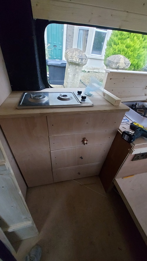 camper van conversion at kitchen cabinetry stage, with DIY wood draws under stove set up on top