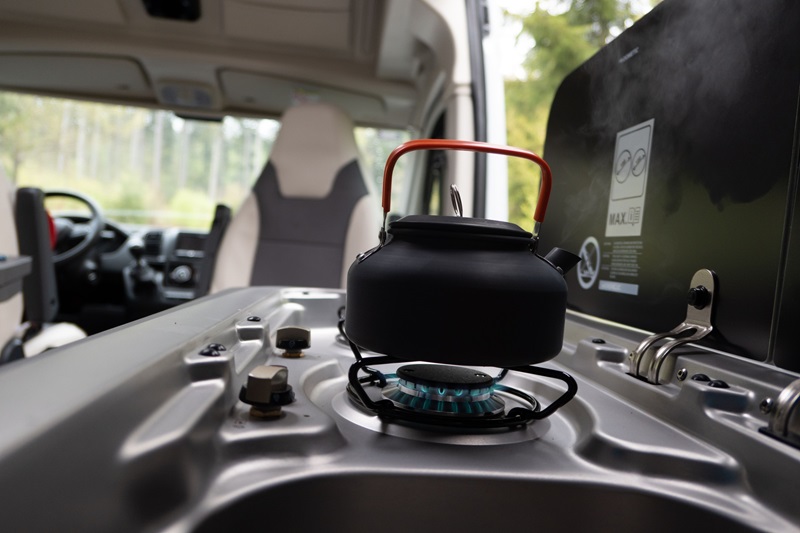 Stove setup in camper van conversion, black kettle on van gas stove.