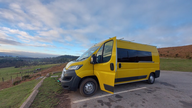 Yellow Peugeot Boxer van parked up over looking across rolling fields in the UK, with passenger door open